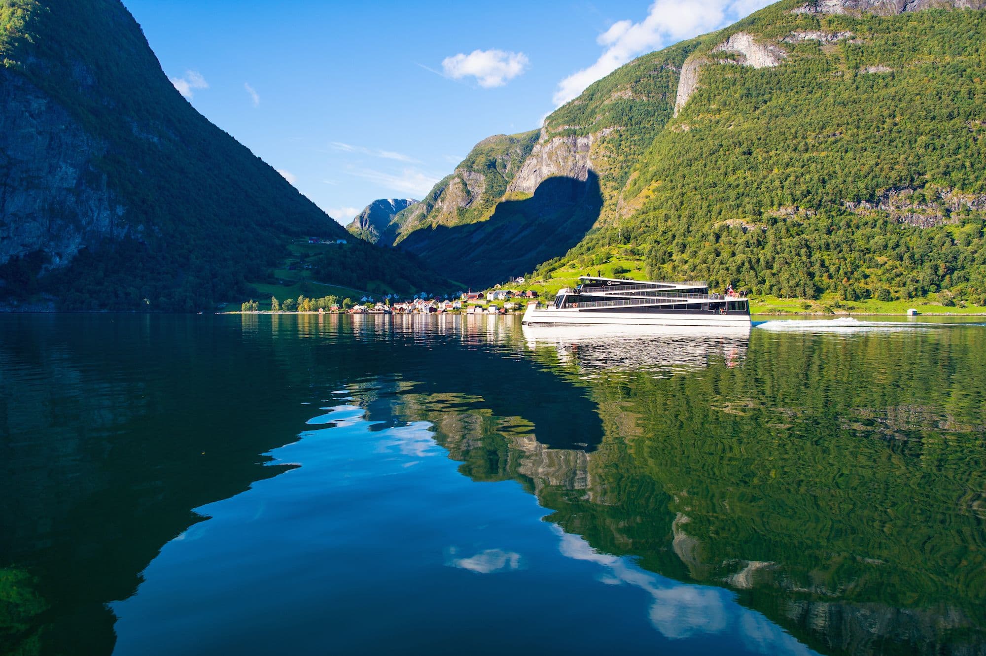 Modern ferry sails calm fjord by green mountains and village.