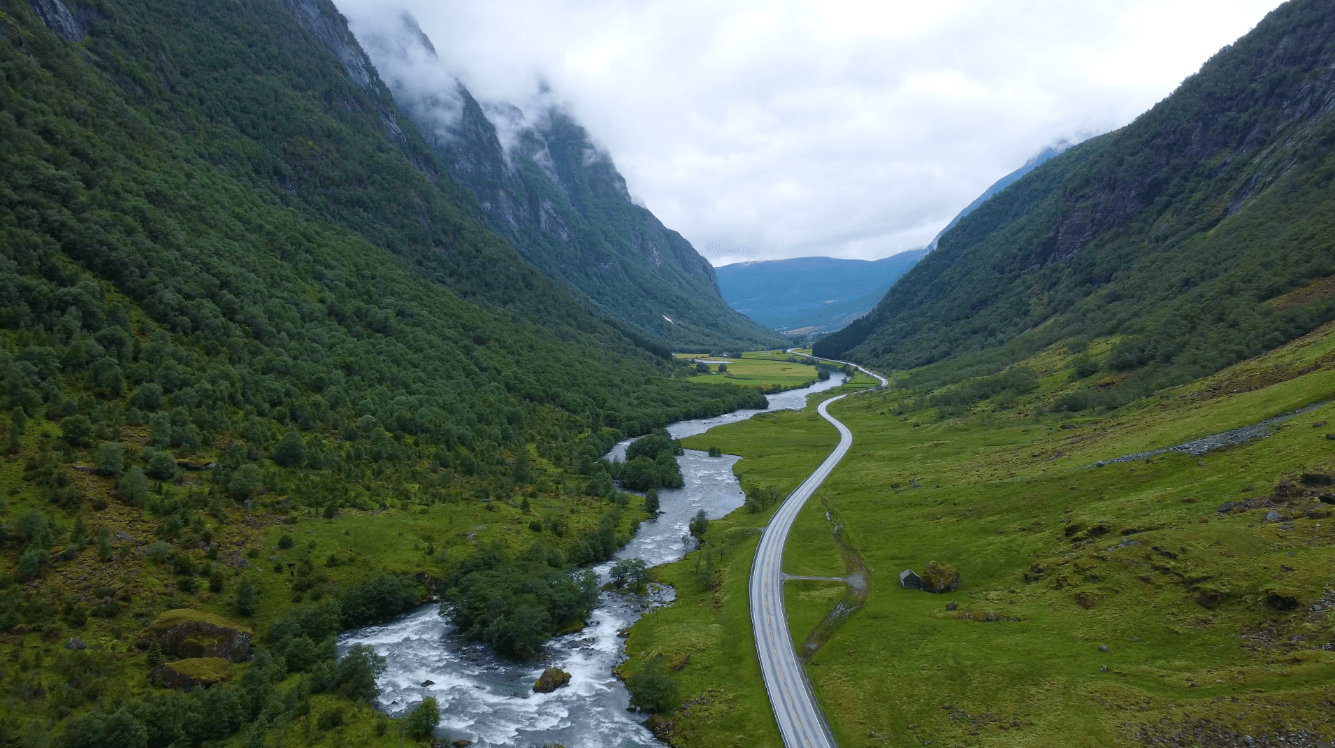 Winding road and river through lush misty mountain valley.