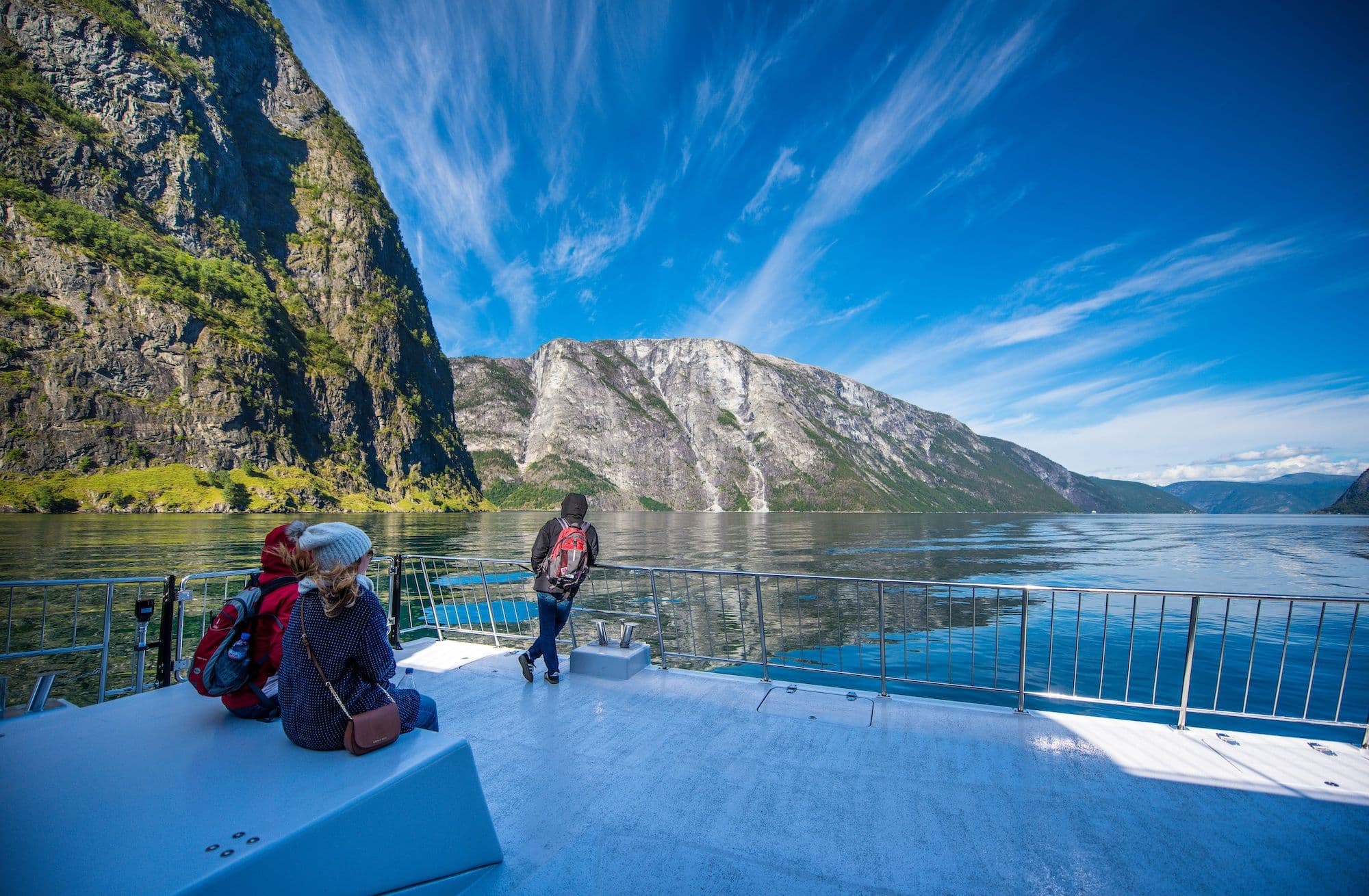 Boat deck passengers enjoy the Nærøyfjord view surrounded by cliffs and wispy clouds.