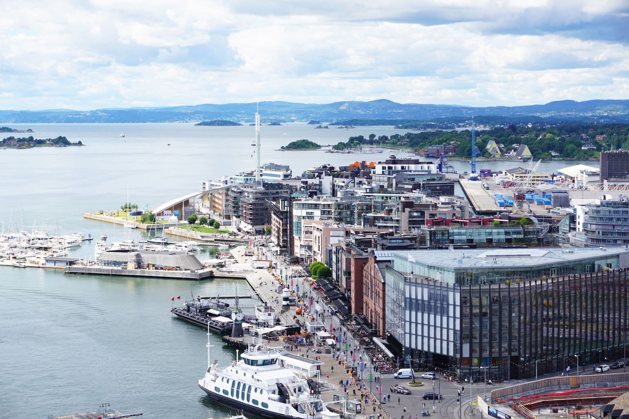 Et livlig Oslo langs vannkanten med moderne arkitektur, yachter og folk som går langs promenaden.