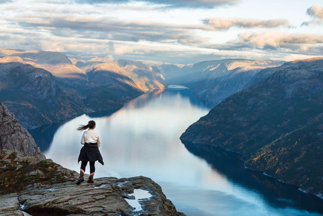 Person i friluftsutstyr på Preikestolen, med utsikt over Lysefjorden, himmelrefleksjoner