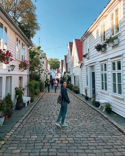 Ung kvinne på spasertur i blomsterdekorert gate i Gamle Stavanger sentrum om sommeren