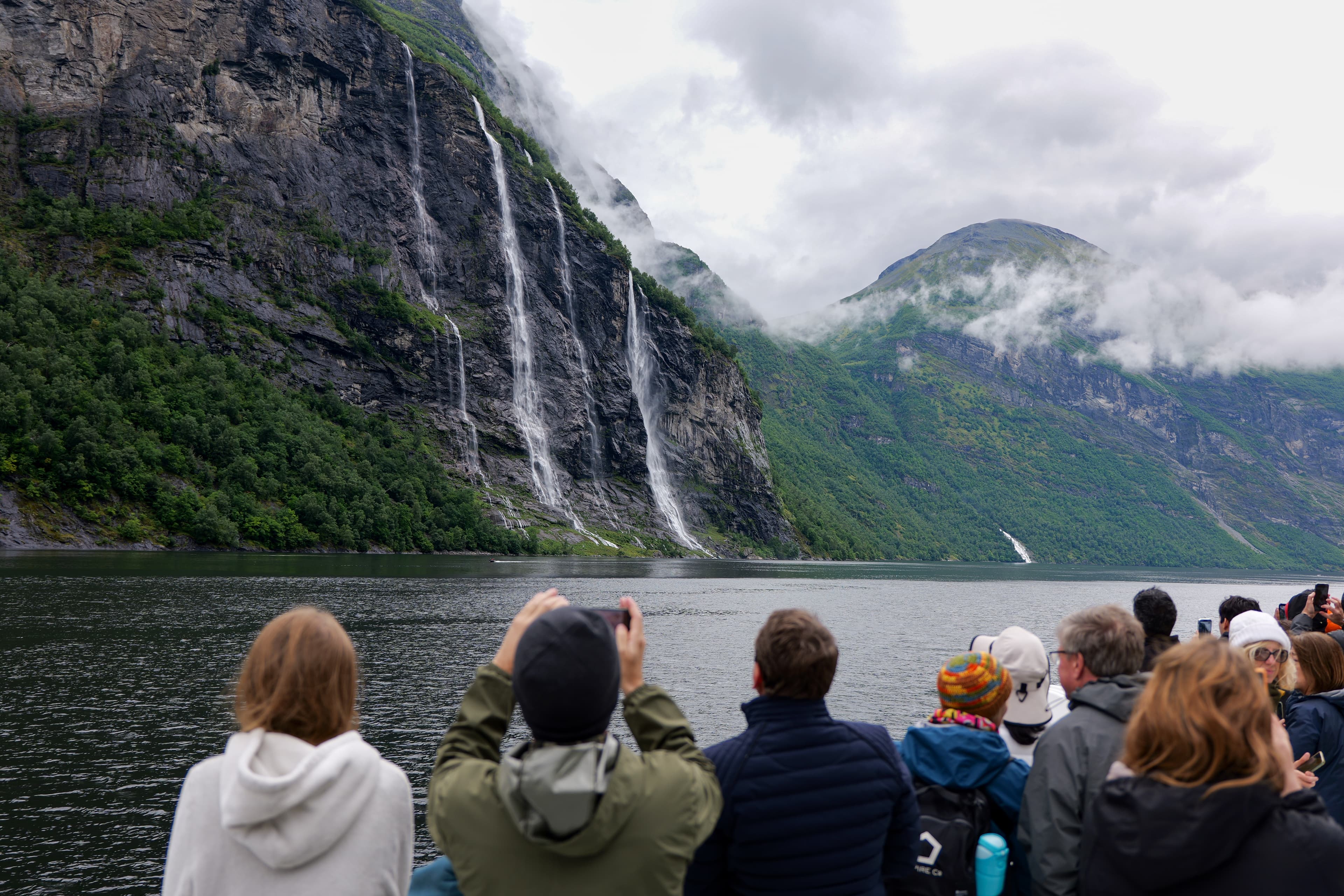 Menschen auf einer Geirangerfjord-Kreuzfahrt fotografieren den Wasserfall Die Sieben Schwestern vom Schiff aus